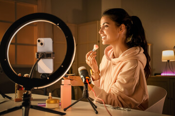 Female beauty blogger with makeup brush and powder recording video at home in evening