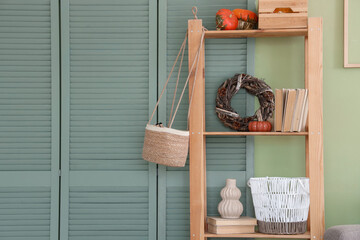 Shelving unit with pumpkins, books and decor near green wall