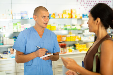 Fototapeta premium Man doctor talking with female client about treatment and writing recipe for her.