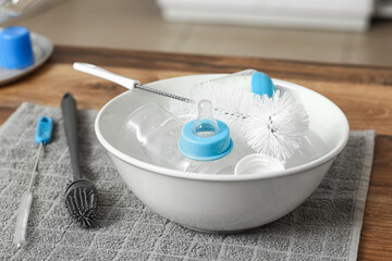 Basin of water with baby bottles and cleaning brushes on counter in kitchen, closeup
