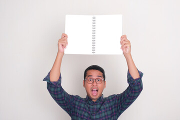 A man showing shocked face while holding blank book pages above his head