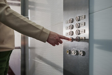 Unrecognizable young woman pressing the button for the ground floor inside a glass elevator with...