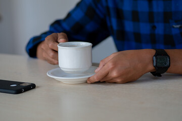 A person in a blue plaid shirt takes a moment for a coffee break, holding a white ceramic cup at a table with a smartphone nearby.