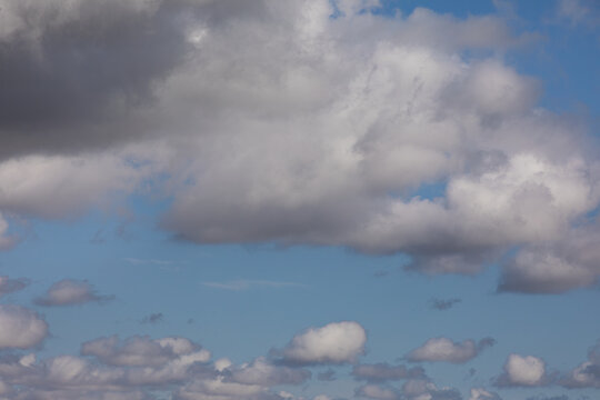 Photo of white and gray fluffy clouds against light blue sky, background texture.