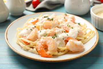 Tasty pasta with shrimps, creamy sauce and cheese on light blue wooden table, closeup