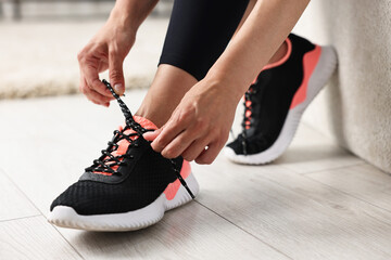 Woman tying shoelace of sneaker indoors, closeup