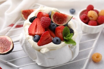 Pavlova cake (meringue dessert) with whipped cream, fresh berries, mint and fig on table, closeup
