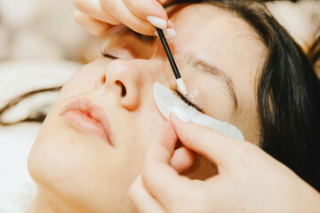 A girl cosmetologist laminates and paints the eyelashes of a teenage client.