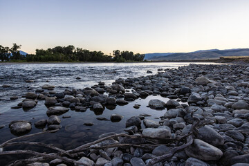 Photograph of Reflective still rocky river shoreline of the Snake River large river rocks
