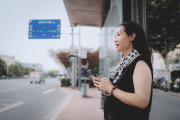 Woman Waiting at a City Bus Stop While Using Her Phone