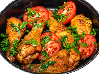 Appetizing chicken thighs baked with tomatoes and greens in a deep black pan