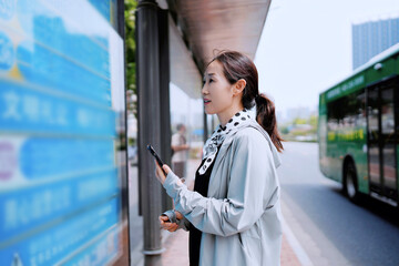 Woman at Bus Stop Checking Schedule with Smartphone in Urban Setting