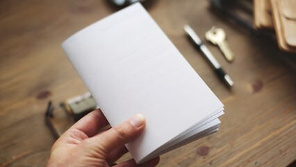 A hand holding a blank white flyer brochure booklet. The booklet has a few pages neatly stacked