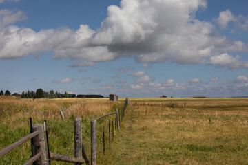 Landscape photo of open ranch field and barbed wire wood post fence on a beautiful peaceful day white fluffy clouds in the sky.