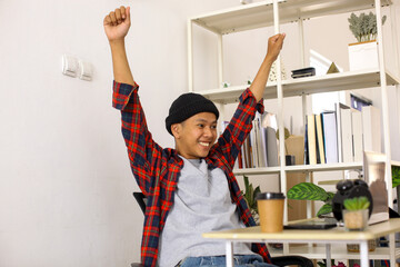 Asian man using laptop computer screaming yes celebrating success while sitting at home office