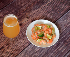 A glass of wheat beer and a plate of peeled boiled shrimp with pieces of lime on a wooden table.