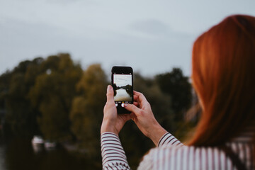 woman holds a phone in her hands and takes pictures of the evening city and bridge