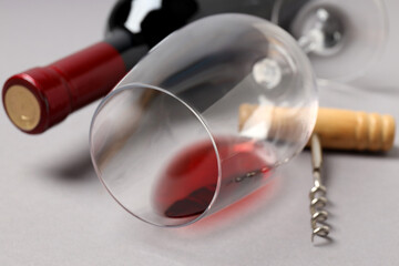 A bottle of wine, a glass and a corkscrew, on a gray background.