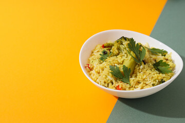 Pilaf with vegetables in bowl on yellow and green background, space for text