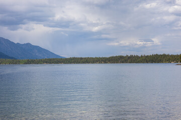 Photo from Jenny Lake at the grand Tetons national park in Wyoming. View of reflective lake surface and cloudy bright sky.