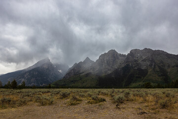 Photograph of cloudy gloomy day grassland field and majestic mountains in the background covered in rain clouds. © Rebecca