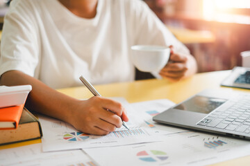 A business professional working on financial reports with a laptop and coffee, highlighting productivity and modern office environment.