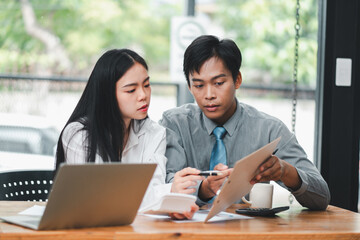 Two young professionals working together on a project in a modern office environment, discussing ideas and reviewing documents.