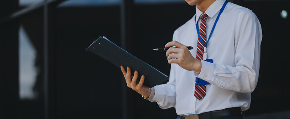 Serious businessman looking at paper documents in front of office building. Focused male manager checking reports before work while standing outdoors.