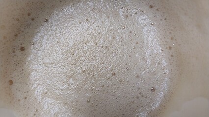 a close-up view of a frothy or bubbly surface, likely the top of a beverage such as coffee or a latte. The bubbles are small and densely packed, creating a creamy texture