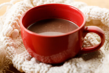 Cup of delicious hot chocolate on warm sweater on wooden table background. Selective focus.