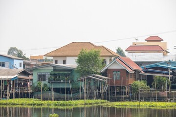 A scenic view of traditional wooden houses on stilts by a calm water body, surrounded by greenery. The architecture reflects local culture, with a mix of colors and styles.