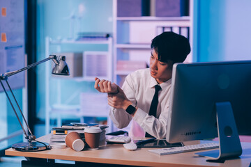 Young pensive asian man working late concentrated and serious in front of computer at night in dark office, Late night working or studying concept.