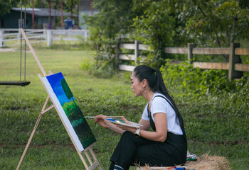 A woman sits and paints in a meadow surrounded by nature.