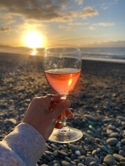 Hand holding a glass of wine with beach views and sunset at the background , glass of wine on the beach