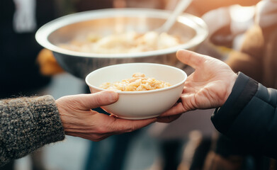 Hands passing a bowl of hot food during a community meal service.