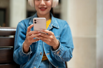 A close-up of a woman in a denim jacket using her smartphone while sitting on a bench in the city.