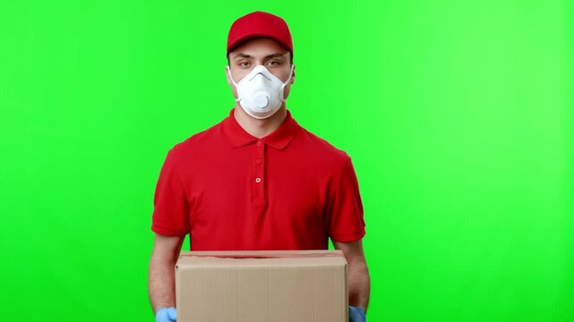 A delivery professional in a red uniform is holding a cardboard box while wearing a protective mask. The bright green backdrop emphasizes the focus on the delivery activity.