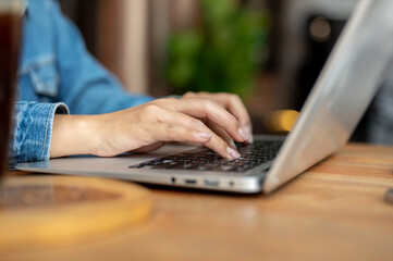 A close-up of a woman working on her laptop in a coffee shop, typing on the laptop keyboard.