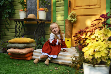 Beautiful little girl of two years old playing in the autumn yard. Little child playing in the yard of the house. Girl with long hair in a dress