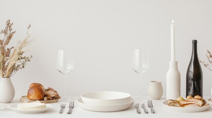 A minimalist dining table set up with plates, glassware, cutlery, bread, a candle, a bottle, and dried flowers for a stylish aesthetic.