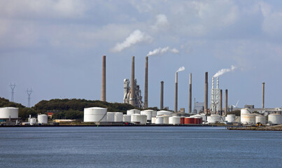 Wide modern cement factory with chimneys puffing out white smoke and the seaside during the production of cement and the sea