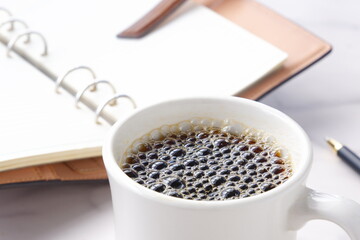 コーヒーとシステム手帳、ボールペンでデスクワークをしているイメージ
