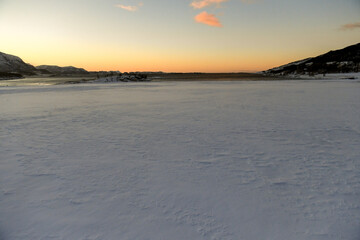 Landscape shot highlighting the rugged mountains and snow-covered beaches of arctic norway during a brief golden hour during the long winters.