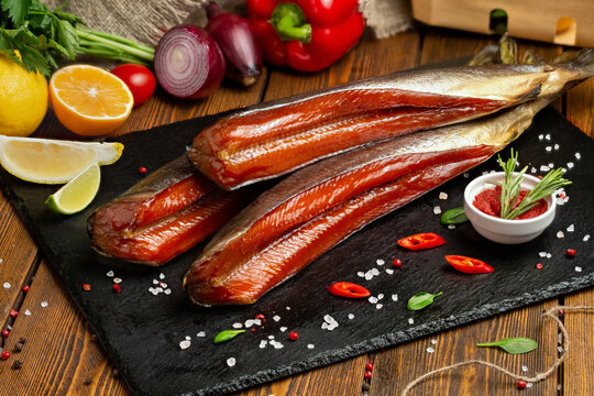 Smoked red fish, fish balyk on a black board with fresh vegetables
