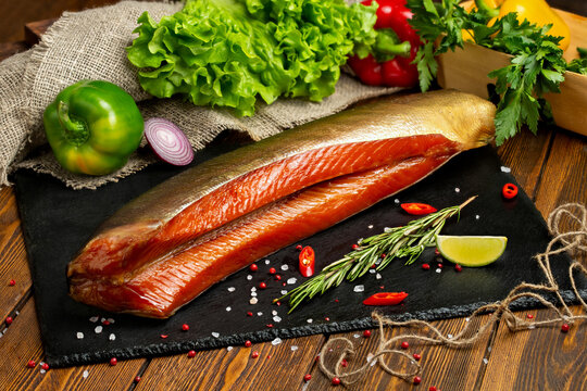 Smoked red fish, fish balyk on a black board with fresh vegetables