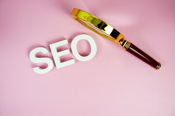 Seo words (Search Engine Optimization) letters with magnifying glass on pink background