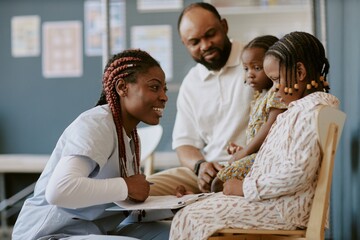 Obraz premium Smiling healthcare worker engaging with a family in a medical setting, showing compassion and professionalism while two children and a parent observe attentively