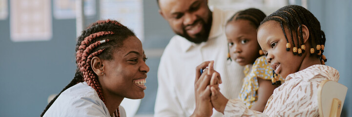 Smiling woman engaging with child while others observe in classroom environment, showcasing...