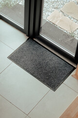 A black doormat placed at an entrance with sliding glass doors leading to a patio area during...