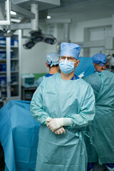Surgical team preps in sterile room. A surgical team in scrubs and masks readies for an operation in an operating room with medical equipment.